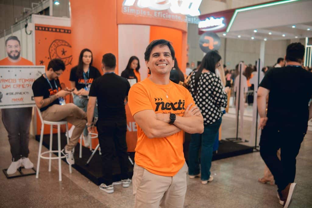 Rafael Praxedes, CEO do Portal Direito do Empregado, em frente ao estante da NEXTI vestido com uma blusa laranja com o nome NEXTI no Ceará RH 2024